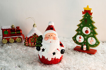 Table covered with snowflakes with Christmas decorations. Santa Claus, Christmas tree with red, gold balls and lights. Selective focus.