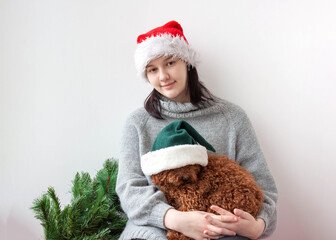 A teenage girl in a Santa hat holds a miniature poodle in her arms
