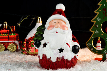 Table covered with snowflakes with Christmas decorations. Santa Claus, Christmas tree with red, gold balls and lights. Selective focus.