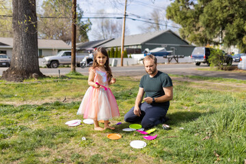 Adorable little girl and her father cutting colorful paper plates in front yard
