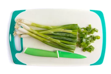 Fotobehang Overhead view of a bunch of green onions or shallots on a White cutting board with a green paring knife with pieces cut off © SockaGPhoto
