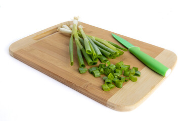 A bunch of green onions or shallots on a wooden cutting board with a green paring knife with pieces cut off
