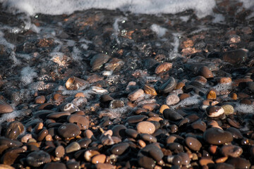 Pebbles on the seashore. Wet pebbles. The surf line. Sea foam. Close-up. Selective focus. Natural background.