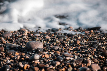 Pebbles on the seashore. Wet pebbles. The surf line. Sea foam. Close-up. Selective focus. Natural background.