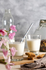 Two glasses and a bottle of milk, cereal bars, some nuts and raisins in a jar and a brown napkin with pink flowers.