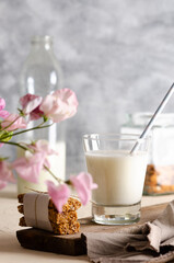 A glass and a bottle of milk, cereal bars, some almonds in a jar and a brown napkin with pink flowers. 