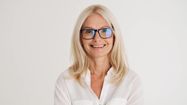 Close-up view of the smiling mature woman putting on glasses in the white studio