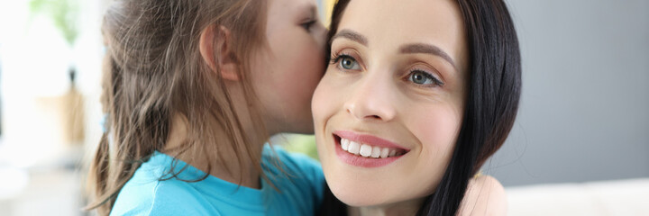Little girl whispers secret in mom ear