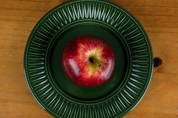 beautiful red and shiny apple served in a dark green plate on the wooden table, photo view from above and close up.