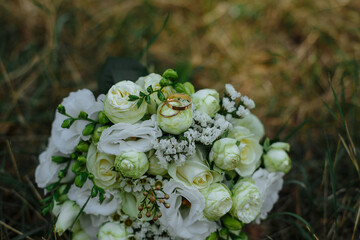 a wedding bouquet with fresh flowers lies on the grass, wedding rings lie on the bouquet