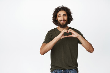Romantic middle eastern guy, showing heart hands gesture and smiling, I love you sign, happy valentines day concept, white background