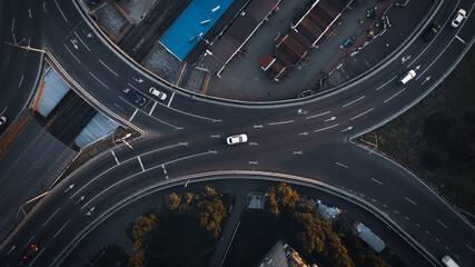 Crossing asphalt roads with a white car: top aerial view. Highway junction in the city in the evening.