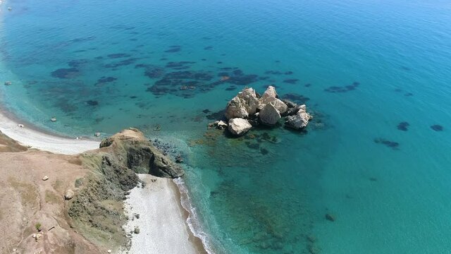 Aerial top view of cliff rocks in a Turquoise water at sunny day. Ocean waves on beautiful beach drone 4k shot. Sea crashing against Lonely mountain rock, Tourist destination on Cyprus