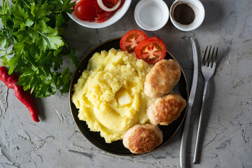 A hearty dinner for the family: Mashed potatoes, pork cutlets, slices of tomatoes on a plate on a gray background. Top view