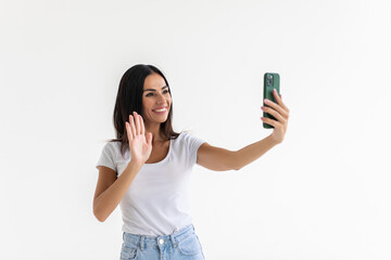 Smiling young woman making selfie photo while waving palm on a white background