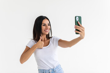 Happy cheerful young woman showing thumb up and making selfie on phone isolated on white background