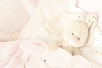 The hare lies on the child's bed. Children's toy rabbit in pink. Childish transparent, blurred...