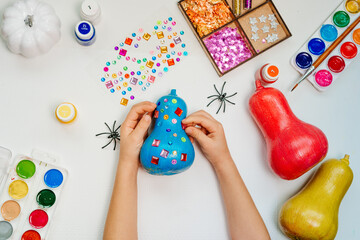 Child decorating colored painted pumpkins with shine stickers.