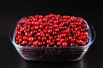 Glass bowl with cranberries on black background
