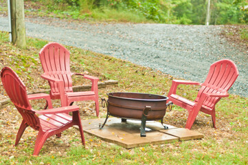 front view, medium distance of a metal, fire pot with three red Adirondack chairs, in front of a cabin in the blue ridge mountains in autumn