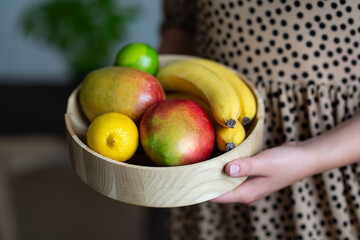 Woman`s hands serving a wooden fruit bowl.
Blurry background. 