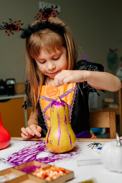 Little girl in whitch costume painting pumpkins at home