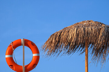 Beach umbrella and lifebuoy on blue sky background. Place for text.
