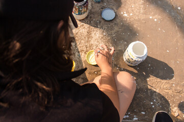 Rear view of a young girl mixing yellow paint on a lid in the street.