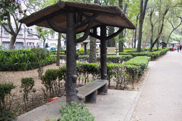Rustic log bench with roof surrounded by bushes in park from Mexico City