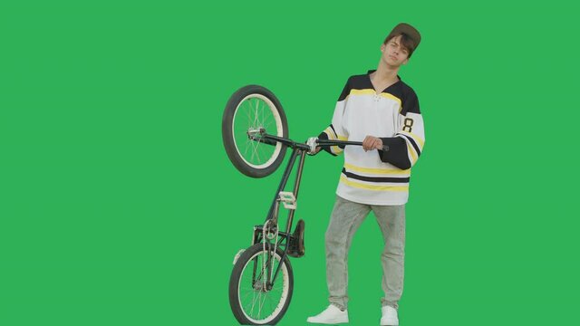 Extreme guy biker wearing hockey jersey standing with bmx bike over green screen background. Sporty young man rider have fun with bicycle on chroma key. 4k raw video footage