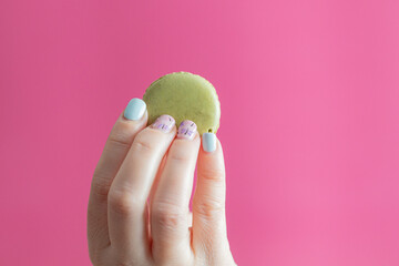 woman's hand with nails painted with green macarons on pink background