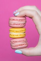 woman's hand with nails painted with three macarons on a pink background