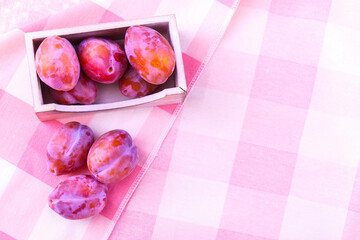 Fresh organic purple plums on a textile background. Ripe tender fruits with a wooden container on the tablecloth