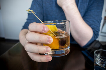Close up of a causcasian male hand holding an old fashioned alcoholic drink inside of a bar and restaurant