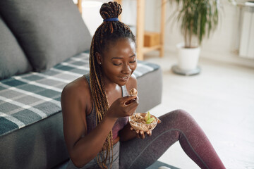 Happy black female athlete eats healthy food while exercising at home.