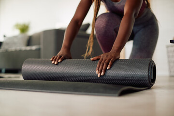 Naklejka premium Close-up of African American athlete rolls up her Yoga mat in living room.
