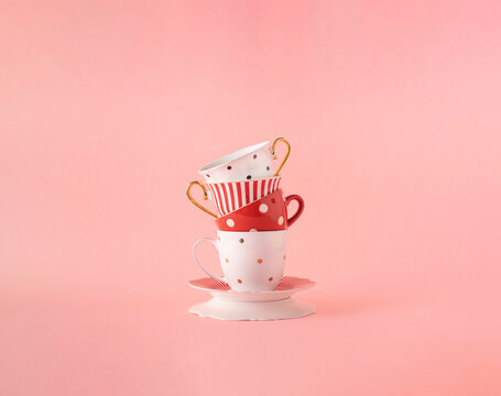Coffee and tea cups and saucers arranged against pastel pink background. Morning routine, pink aesthetic, polka dot pattern.