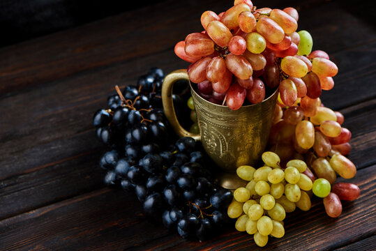 Various grapes in a metal glass on a dark wooden background
