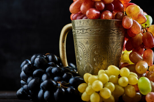 Various grapes in a metal glass on a dark wooden background