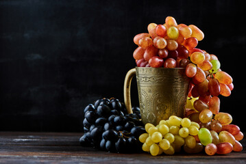 Various grapes in a metal glass on a dark wooden background