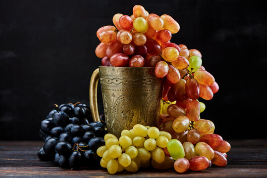 Various grapes in a metal glass on a dark wooden background