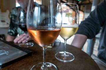Close up focus on a glass of rose wine and white wine at a table where friends and family have gathered for wine tastings