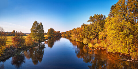 Fall colorful trees reflecting in water, picturesque background. Wild forest, river, meadow sunset panorama
