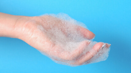 Fototapeta premium Bubble bath foam in woman's hands. Closeup woman's hand washing with soap on a blue background , selective focus. Practice good hygiene. Hygiene and health protection