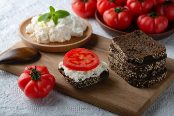 Slices of rye bread with cottage cheese and tomatoes on wooden plate on white background