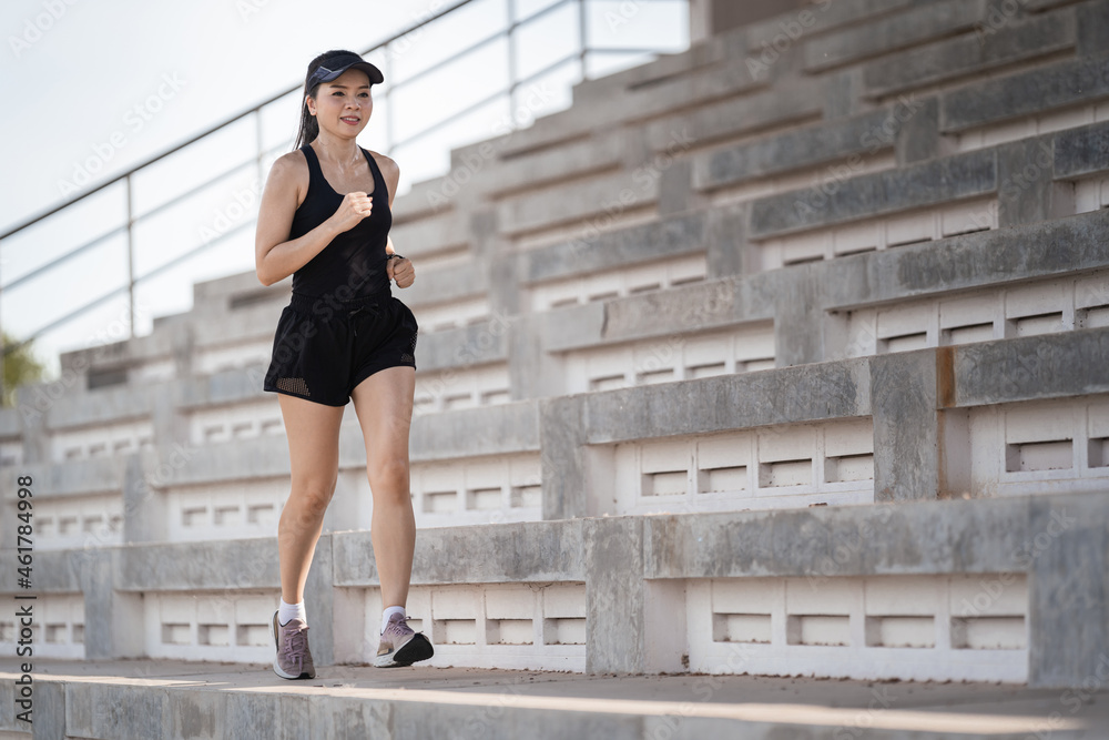 Sticker Healthy adult Asian female running up on concrete stairs of the city stadium