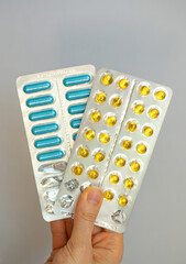 Yellow and blue complex of vitamins and minerals in a blister pack in hand. Focus on the pills