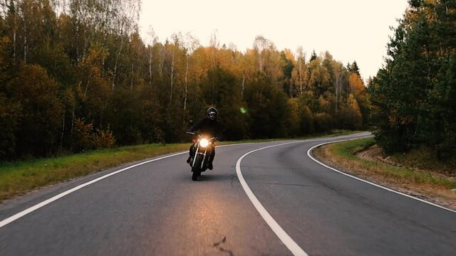 biker rides a vintage retro motorcycle along a scenic forest road in autumn.