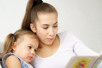 Happy family young mother babysitter hold read book relax embrace cute little children daughters, smiling parent mum tell small kids funny fairy tale story sit on sofa having fun together at home
