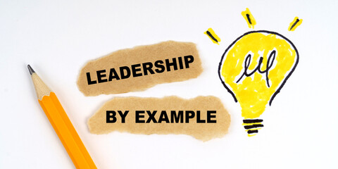 A lamp is drawn on a white sheet, there is a pencil and scraps of paper on which it is written - LEADERSHIP BY EXAMPLE